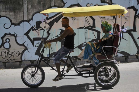 Un hombre lleva a una mujer en su triciclo-taxi en La Habana. | Reuters