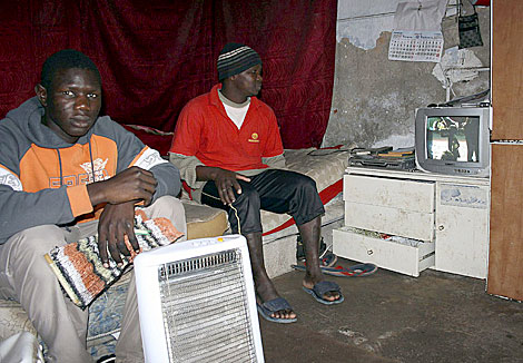 Gora y Abdulah ven la tele, en el garaje semiderruido donde viven. | Miguel Cabrera
