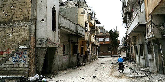 Un niño monta en bicicleta por una calle destruida de Homs. | Efe